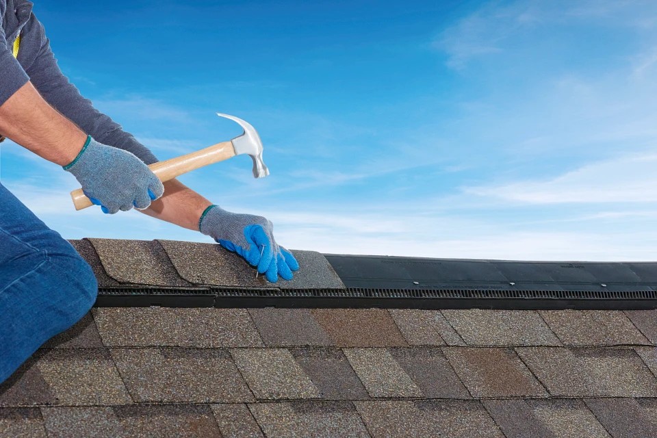 Shows roofer installing shingles over a vented ridge cap.